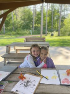 Two girls drawing flowers and embracing while seated at a picnic table